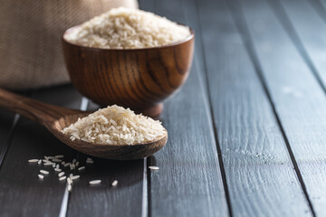 Uncooked white rice on wooden spoon on black table.