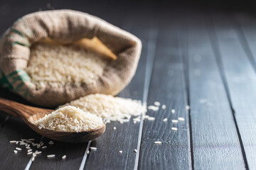 Uncooked white rice on wooden spoon on black table.