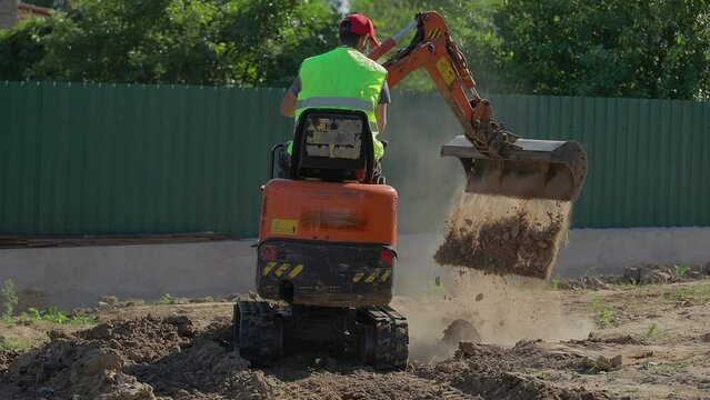 A man on a mini-excavator levels a piece of land, loosens the soil
