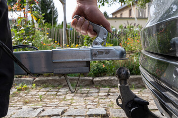 man's hand checks the fixation of the trailer closed hitch lock handle on the towing ball towbar of the car closeup, the safety of driving with a trailer on the road