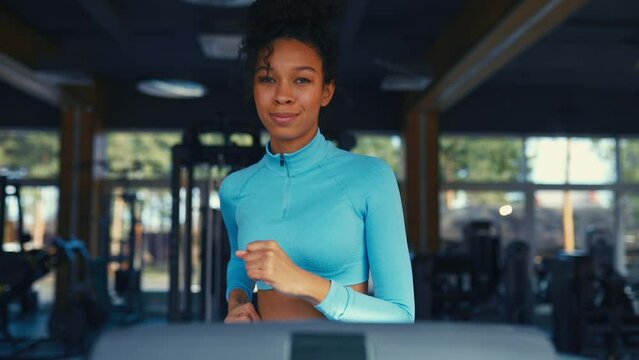 A slender African American girl in sportswear does a cardio workout on a treadmill in the gym. Running activity. The concept of sports and recreation.