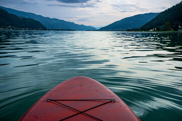 red SUP board on lake Ossiach in Austria with view of mountains in the evening just before a...