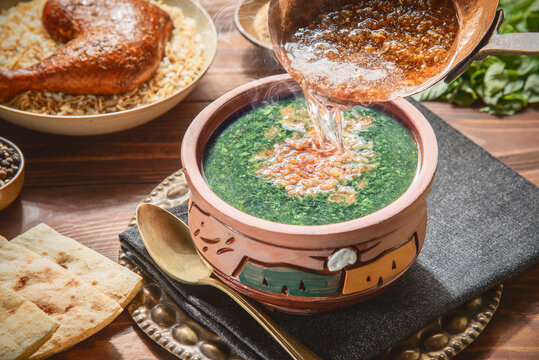 Arabic cuisine: Pouring fried golden garlic over a delicious stewed Molokhya . Traditional Egyptian meal served with rice, chicken, and pita bread on rustic wooden background.