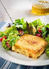 Delicious croque monsieur with lettuce and cherry tomato salad, on a wooden table