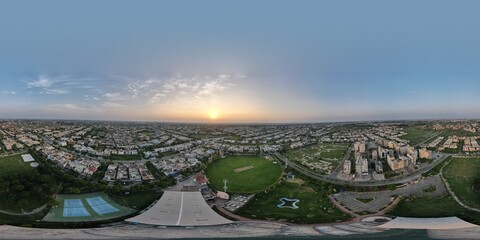 An aerial view (360-degree panorama) of a housing society and its cricket ground at dusk in Lahore, Pakistan.