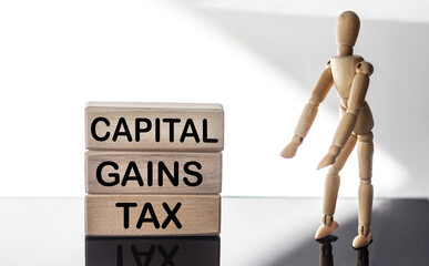 CAPITAL GAINS TAX - words on wooden blocks on a white background, next to a wooden doll. Business and hybrid working culture concept, copy space.