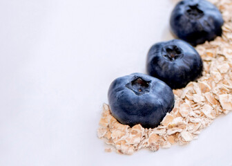 Blueberries and oatmeal flakes in a white plate on a gray background top view. Healthy and wholesome food.