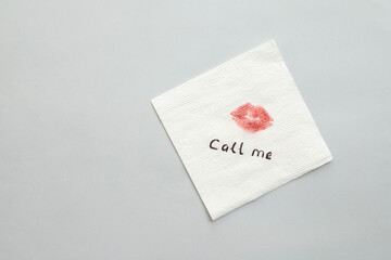 Paper napkin with lipstick mark and words CALL ME on grey background, top view. Space for text