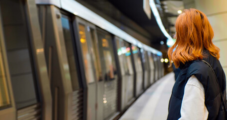 Tourist female waiting at platform of metro station looking at passing train. Busy city people....