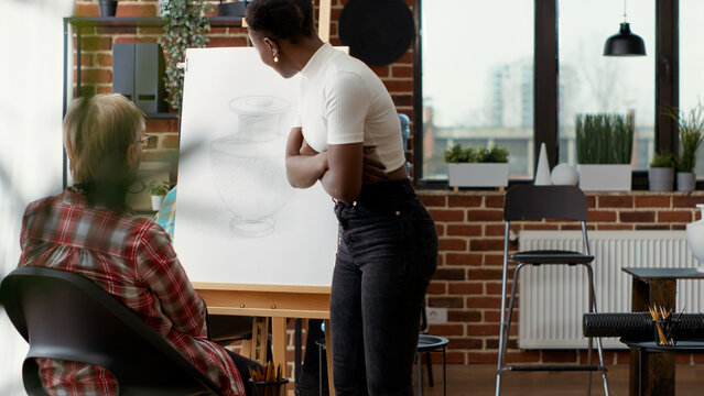 Art teacher training senior woman to draw artwork in art class program, using creativity and artistic instruments. Drawing lesson practice on canvas to learn new skills for development.