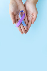 World Autoimmune Arthritis Day. Adult hands holding blue purple ribbon on blue background. RA rheumatoid arthritis illness disease. copy space.