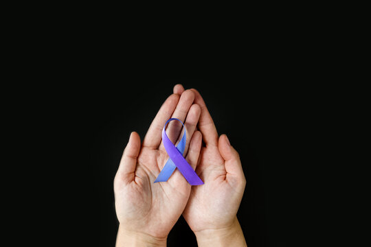 World Autoimmune Arthritis Day. Adult hands holding blue purple ribbon on black background. RA rheumatoid arthritis illness disease. copy space. banner
