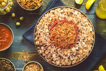 Arabic cuisine; Traditional Egyptian food: Delicious Kushary or Koushari of rice, pasta, chickpeas, lentils, crispy fried onions, fresh lemon and tomato garlic sauce on a plate. Top view with close-up