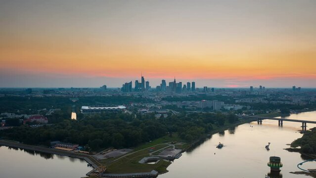 Aerial time lapse hyperlapse modern downtown view during sunset, golden hour cityscape, skyline. Warsaw city panorama and Vistula river backlit with warm evening sun light. Drone shot, urban scene