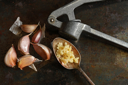 Fresh organic garlic cloves, garlic press and ground garlic in silver spoon on dark grunge background.