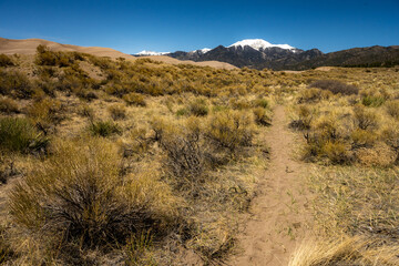 Dirt Trail Heads up Dune Toward Snow Capped Mountains