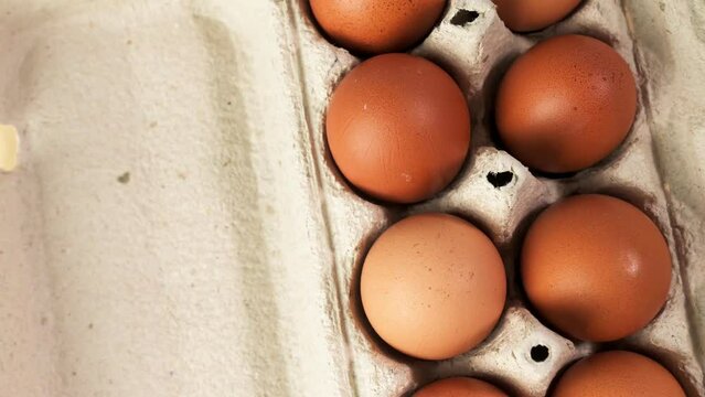 Chicken eggs in a package on a wooden table rotate overhead view.