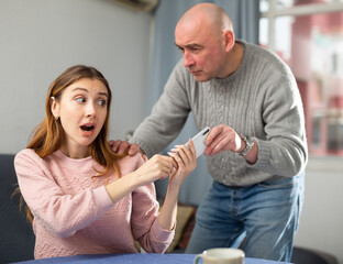 Fototapeta premium Wife and husband having quarrel at home. Man trying to take her phone away.