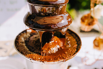 Hot brown milk melted chocolate is poured over the tiers of a fondue fountain close-up. Photo of food, dessert.