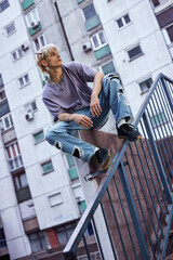 A teenage boy sits on the concrete wall in the urban exterior, looking away and feeling lonely.