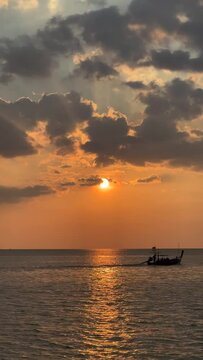 Vertical shot of a long tail boat with tourists enjoying the sunset at Andaman sea, Phuket, Thailand