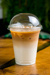 ice latte in a clear disposable cup on wooden table, vertical