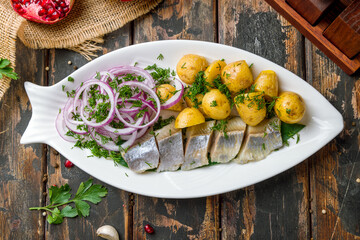 Sliced Herring with mini potatoes and red onion on white plate top view on old wooden table