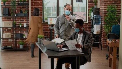 Business men with face mask doing teamwork on startup project, working with data charts and statistics to plan corporate presentation. Diverse people at office job during pandemic. - Powered by Adobe