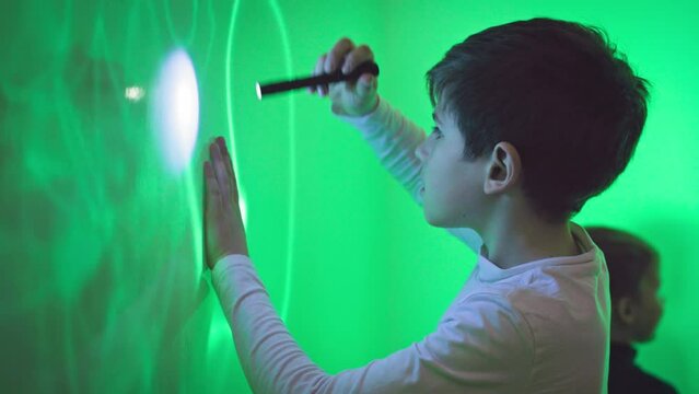 modern education of children, interested boy draws a pattern with an ultraviolet flashlight on a green wall in an interactive room