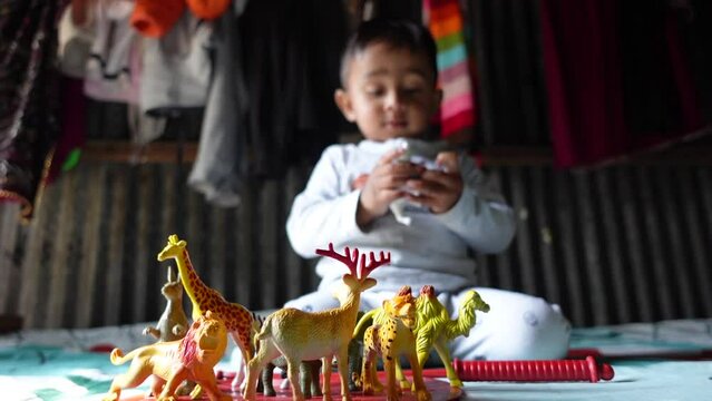 A toddler baby boy is playing intensively with some plastic animal toys. Little boy playing with plastic toy animals at home. Close-up view. Slow motion video. 