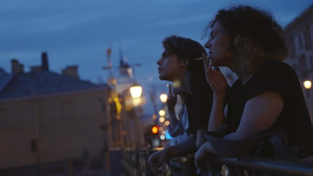 A group of friends stand on the bridge and smoke and talk. Profile. Night city. Slow motion 4k footage