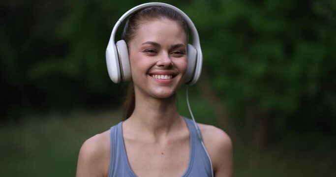 Woman wearing big white headphones listens to her favorite music while working out in nature and smiles with happiness and lifestyle