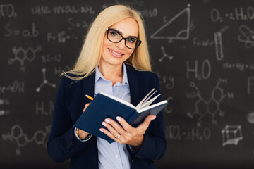 Portrait of happy blonde teacher woman standing near the blackboard in the classroom.