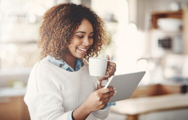 Relaxed, happy and carefree black woman reading social media or news while having coffee at home. Smiling African American female enjoying a quiet morning streaming online or browsing the internet