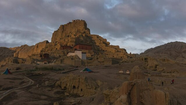 Time-lapse of dark sunrise clouds moving over the ruins of Guge with people camping nearby