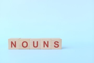 Nouns concept in English grammar education. Wooden block crossword puzzle flat lay in blue background.
