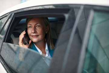 Beautiful Businesswoman is Commuting from Office in a Backseat of Her Luxury Car. Senior Entrepreneur Using Smartphone while in Transfer Taxi in Urban City Street