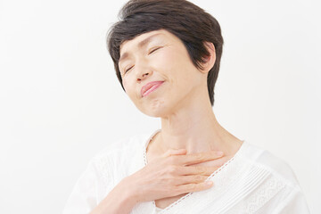 胸元をマッサージするシニア女性　白バック