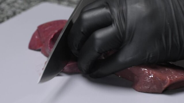 A chef cuts a raw pork liver on a plastic board with a knife. The camera is moving.