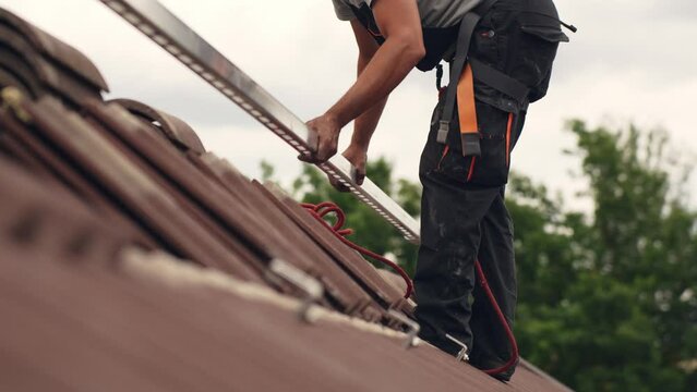 Ground level view of roofer worker adding mounts for solar panel home, day