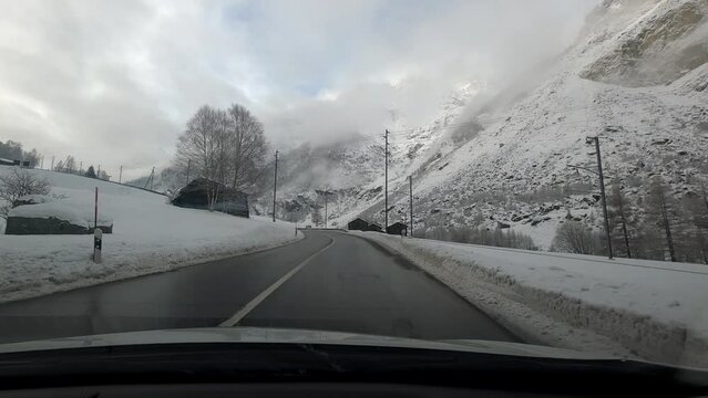 Car travel to Zermatt in winter in bad weather. The road is clear of snow but the landscape is covered with snow.