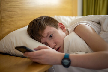 Teen boy reading his phone on the bed. Set an alarm