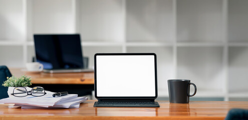 Blank white screen digital tablet with magic keyboard on wooden table in modern office room.