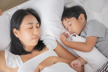 Young Asian woman and son sleeping in her bed and relaxing in bedroom. they are lying on the side and relax with their eyes closed