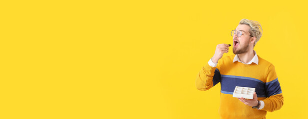 Young man with box of chocolate candies on yellow background with space for text