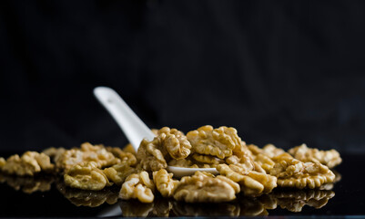 peeled walnuts in a ceramic spoon on a black background with mirror reflections, seasonal nuts, vegan, desserts