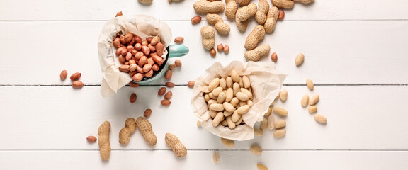 Cups with tasty peanuts on white wooden background