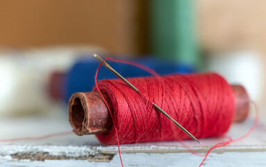 Needle with thread and spool of thread. Soft background.