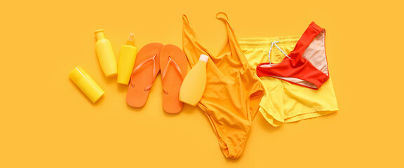 Stylish swimsuits with flip-flops and sunscreen on yellow background