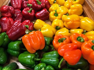 A closeup photo of green, yellow, orange and red bell peppers at a market